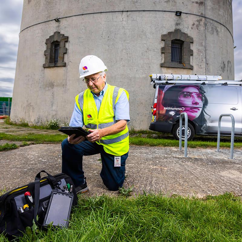 工程师跪在地上，旁边放着一袋工具, outside a tower in Essex County Council, while looking at an electronic tablet